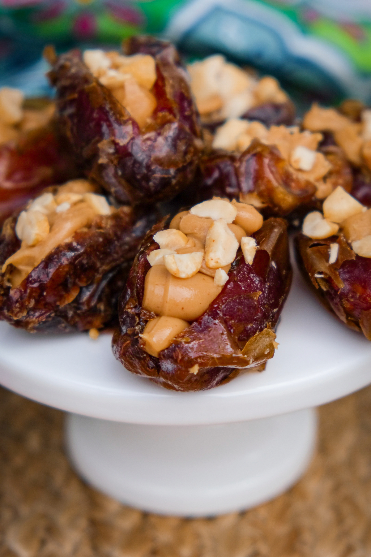 Dates stuffed with peanut butter and topped with chopped peanuts on a small white pedestal plate.