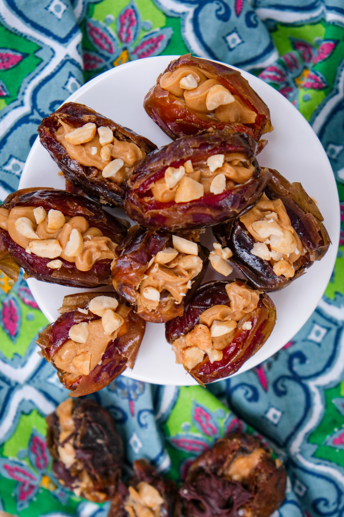 Dates stuffed with peanut butter and topped with chopped peanuts on a small white pedestal plate.