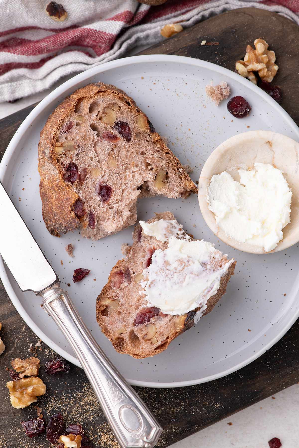 Top view of a slice of bread with cranberries topped with whipped butter on a white plate. 