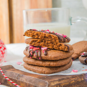 Four chocolate sugar cookies on top of each other on a brown cutting board.