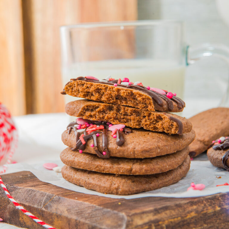 Four chocolate sugar cookies on top of each other on a brown cutting board.