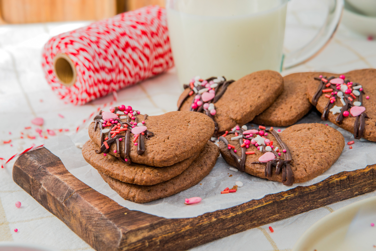 Hear shaped chocolate sugar cookies topped with chocolate drizzle and pink and red sprinkles on the corner of the heart.
