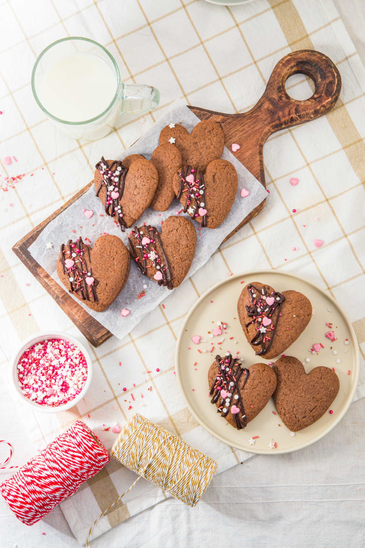 Overhead view of chocolate heart shaped cookies on a serving plate and cutting board lined with white parchment paper.