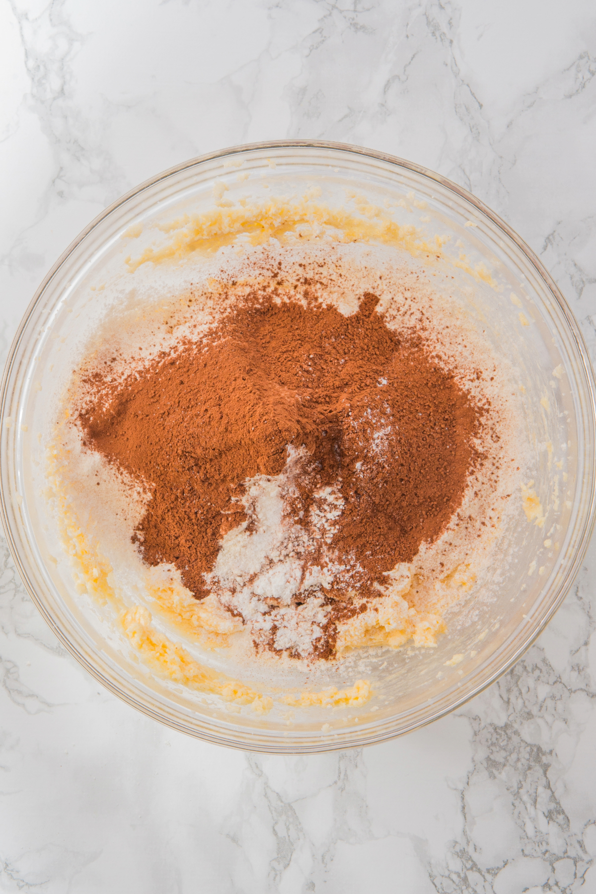 Flour and chocolate added to creamed butter and sugar in a mixing bowl to make cookie dough.