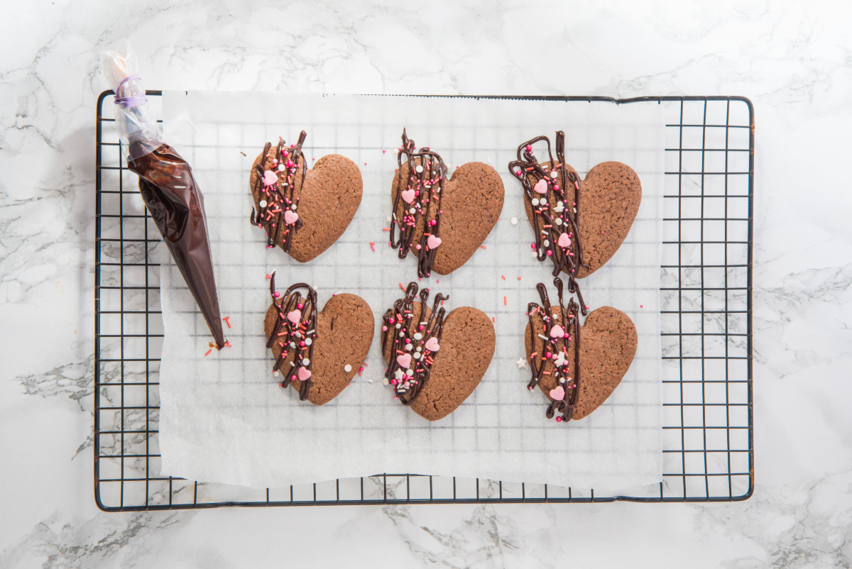 Cooled chocolate shaped cookie on a cooling rack decorated with a drizzle of chocolate and colorful sprinkles.