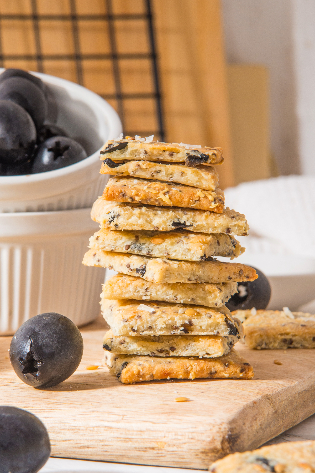Homemade low carb crackers with chopped olives on a wooden cutting board.
