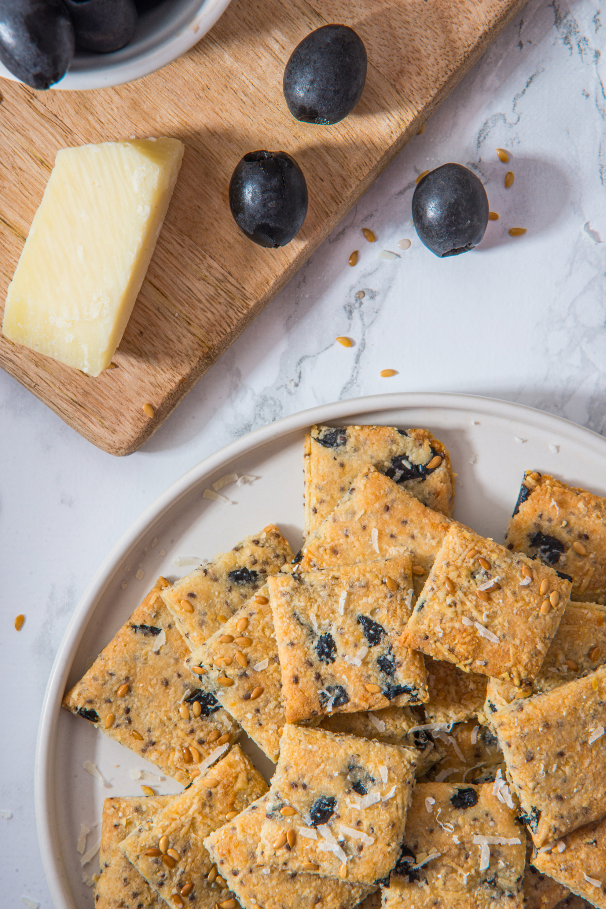 Top view of homemade low carb crackers on a plate with a bowl of fresh olives on the side.