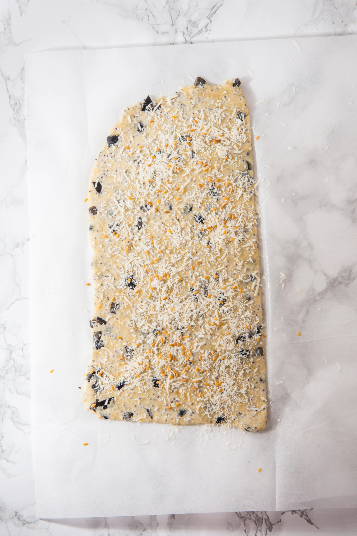 Homemade cracker dough rolled flat between two sheets of parchment paper.