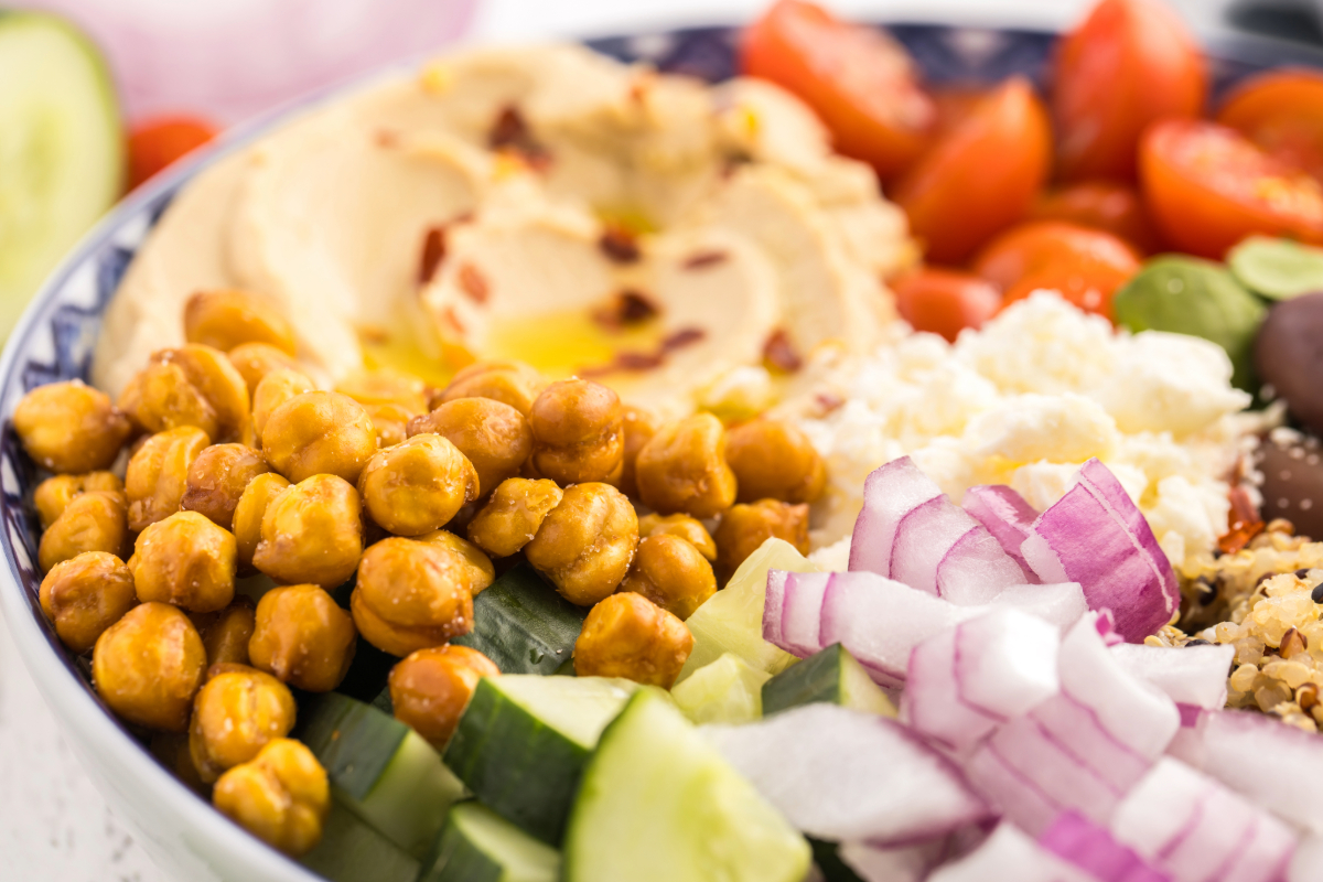 Healthy bowl of salad ingredients with crunchy chickpeas, hummus, feta, cucumbers and diced red onion.
