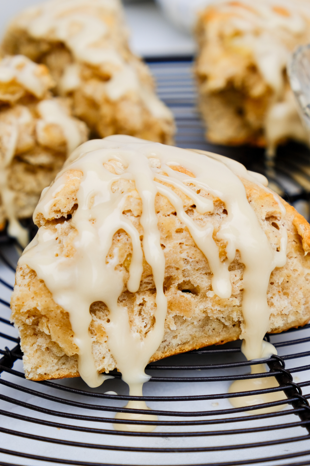 Banana scones on a black cooling rack with maple glaze drizzled on top of the scone.