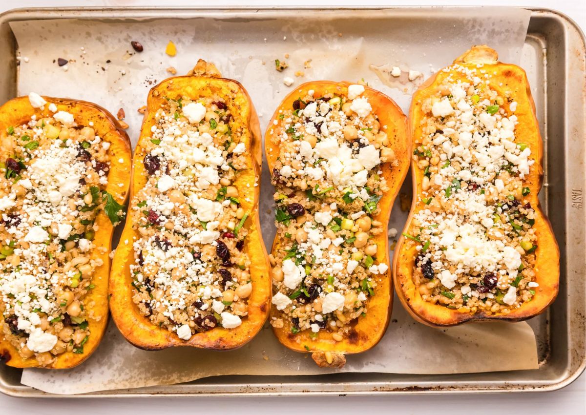 Four halves of mediterrean stuffed butternut squash on a baking sheet.