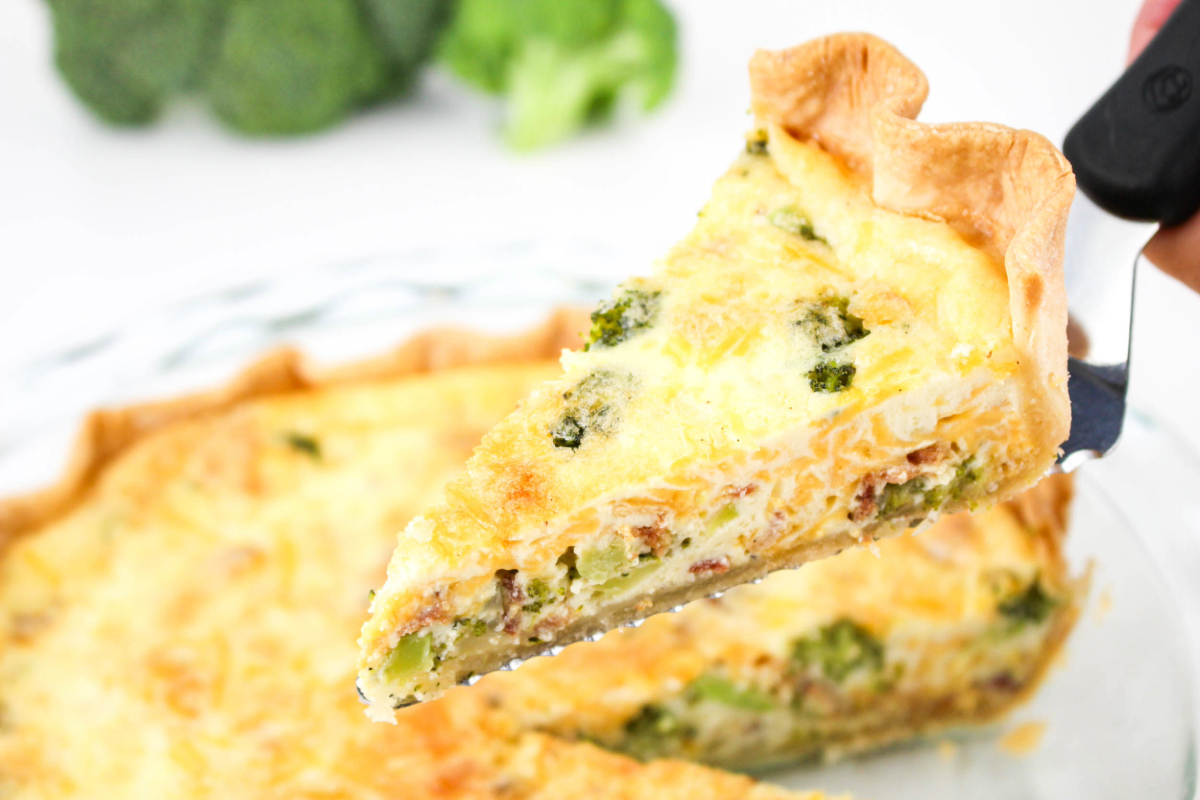 A slice of quiche on pie server over a pie dish.