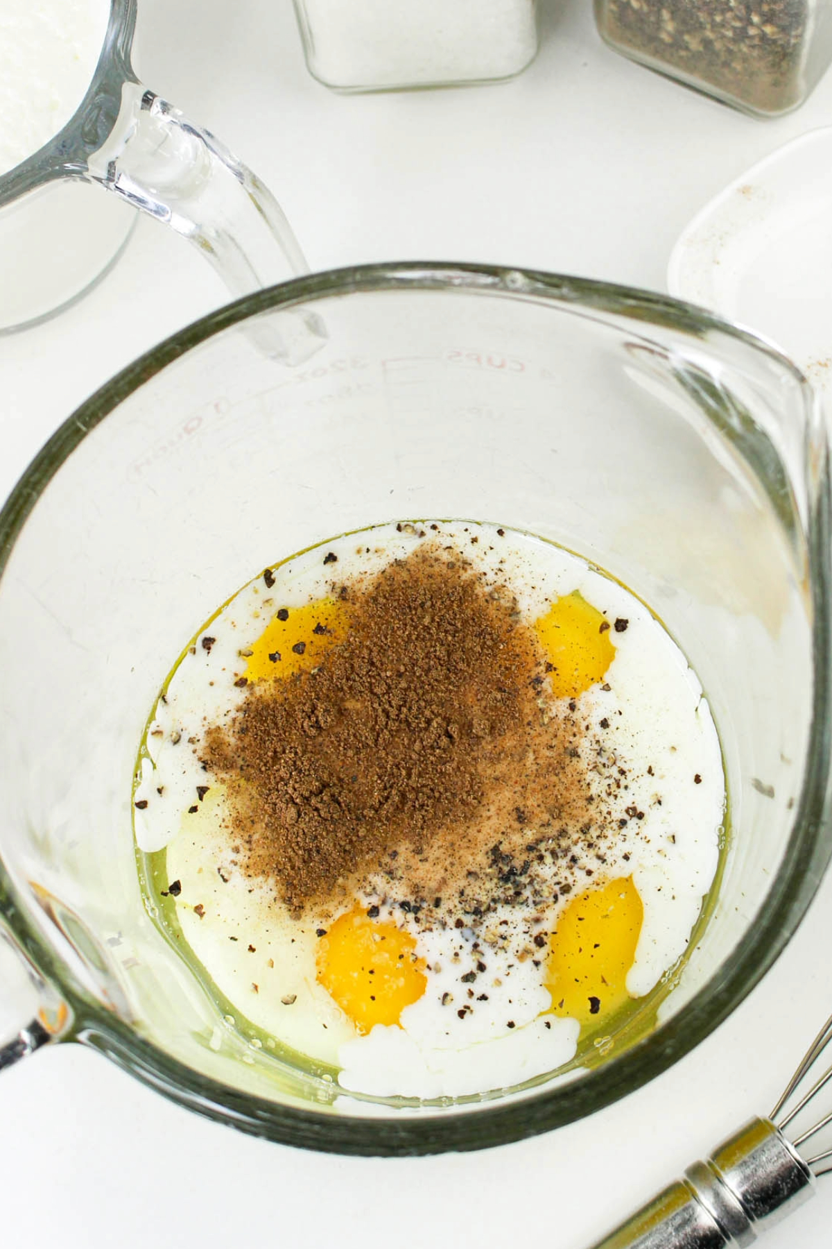 Eggs, cream, and spices for quiche filling in a large mixing bowl before whisking together.