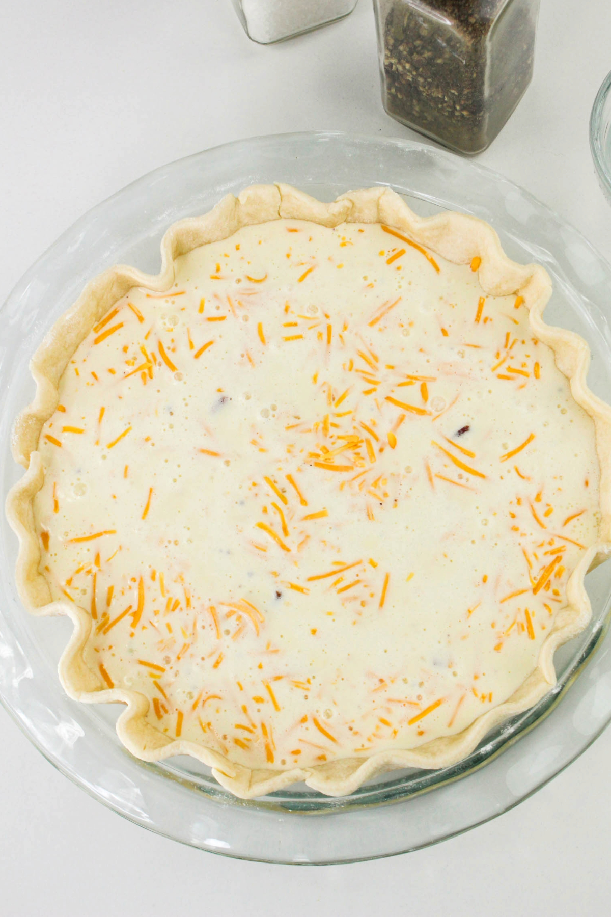 Unbaked quiche with shredded cheddar cheese in a pie plate before baking.