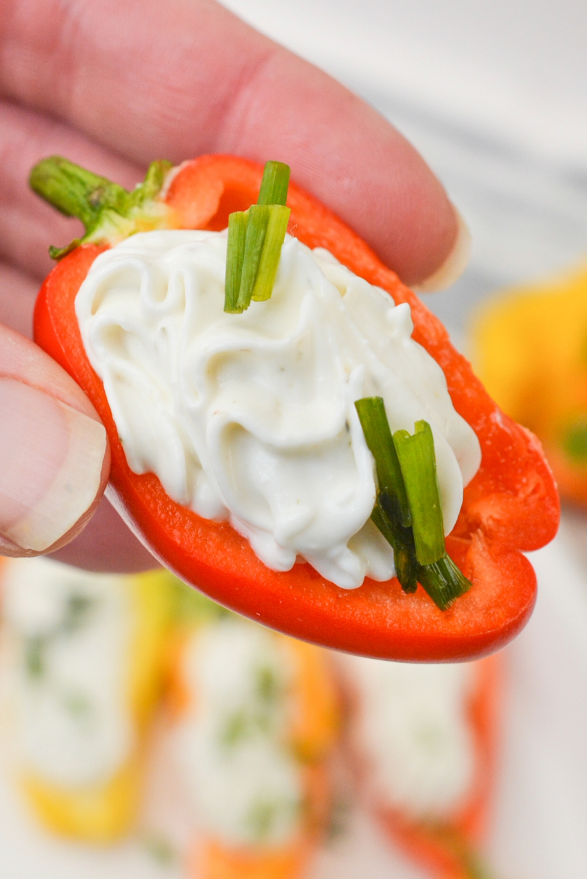 A hand holding a mini pepper stuffed with goat cheese ready to eat.