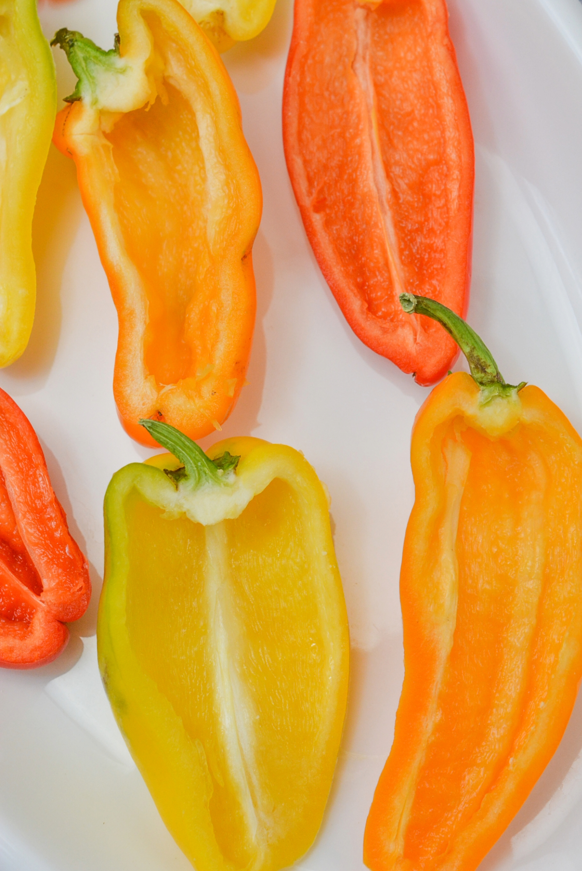 Mini peppers sliced in half and seeded on a white plate.