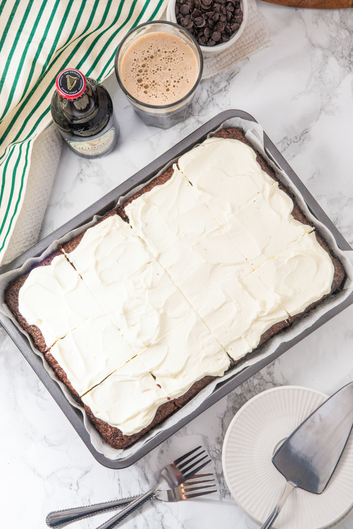 A top view of a whole cake in a silver baking pan topped with cream cheese frosting.