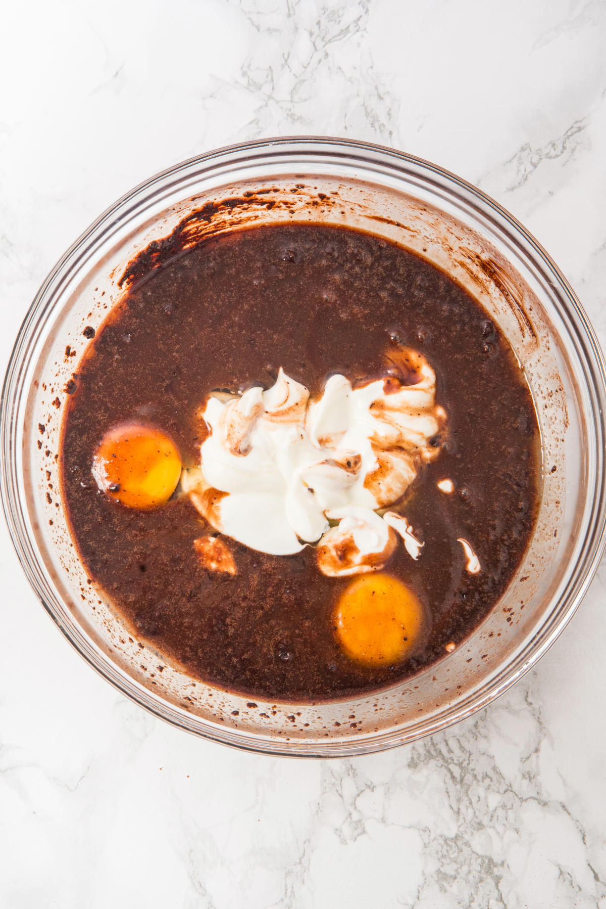 Chocolate cake batter in a clear mixing bowl with eggs before blending together.