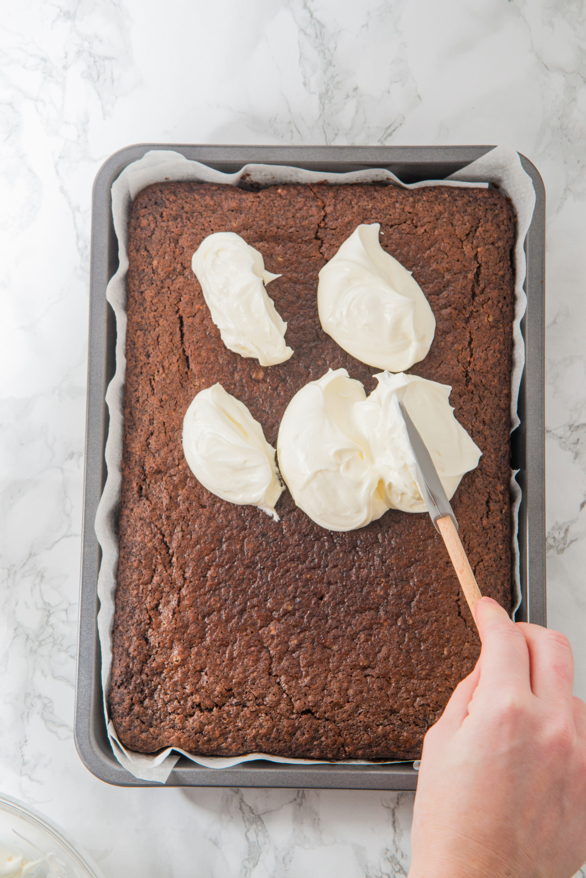 Cream cheese frosting is added to a chocolate sheet cake before spreading it evenly.