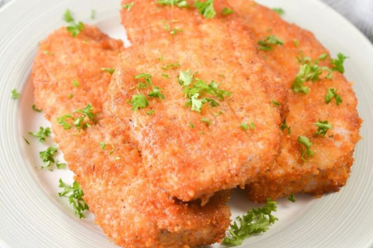 Three shake and bake pork chops on a white plate sprinkled with fresh parsley.