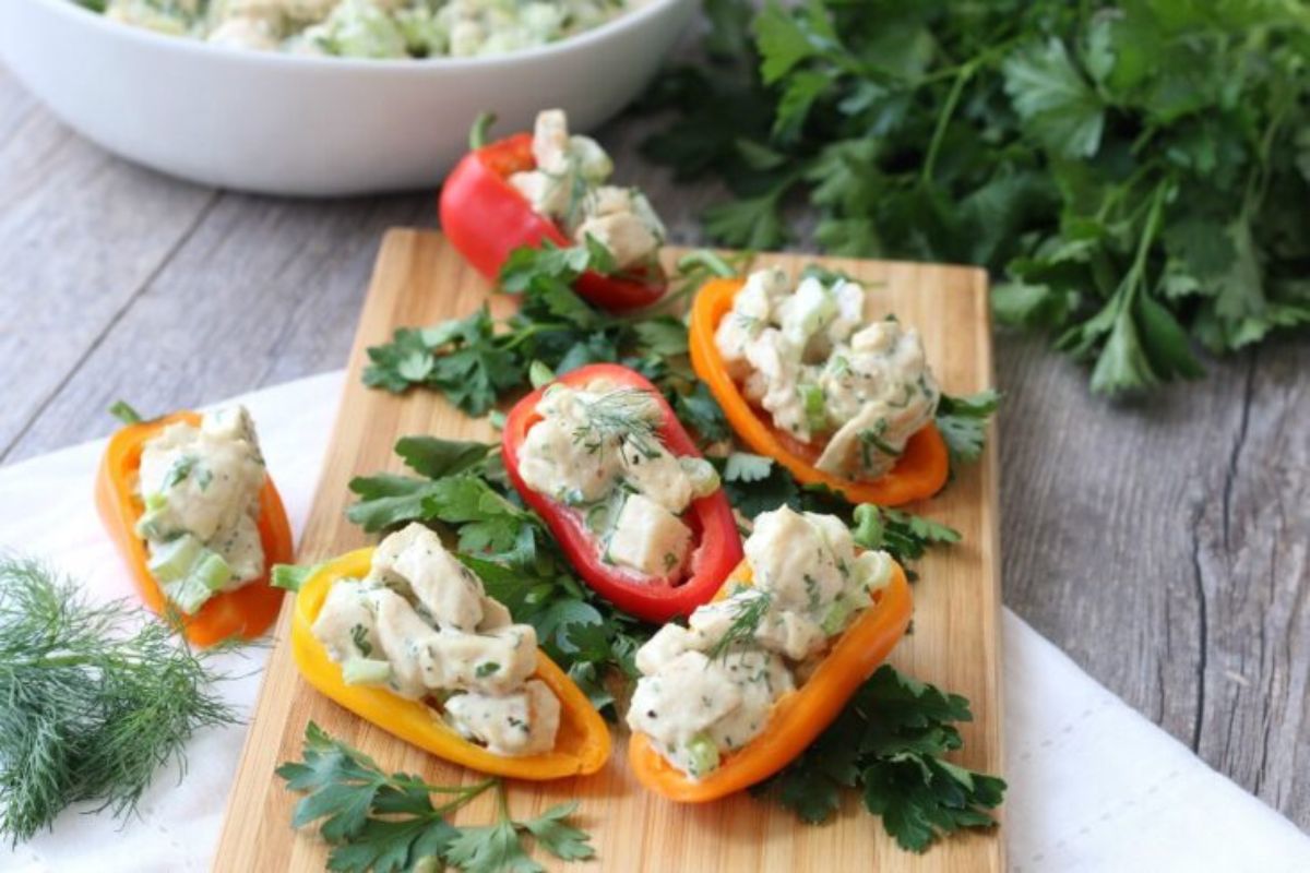 Colorful bell pepper halves filled with a creamy chicken salad are arranged on a wooden board.