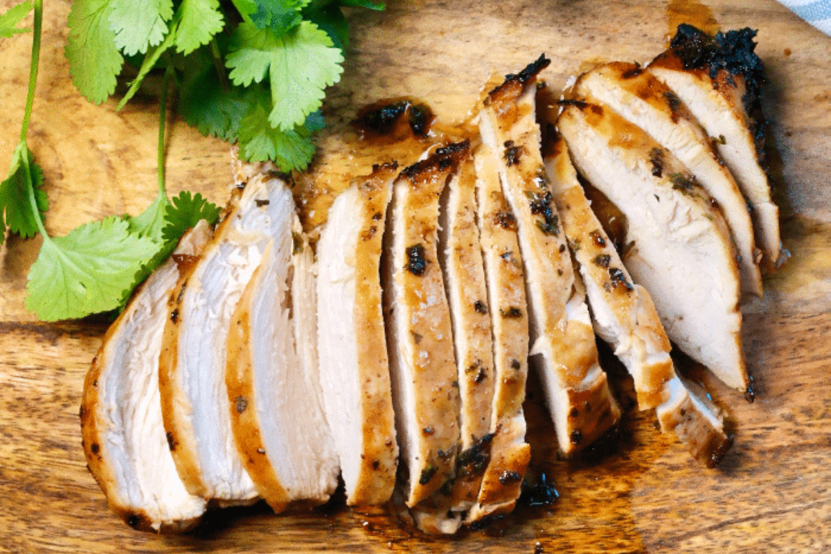 Chicken breast cooked in an air fryer sliced and resting on a wood cutting board. 