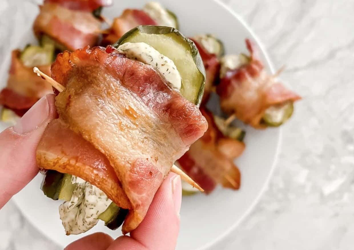 Bacon wrapped pickle bite held in a woman's hand.