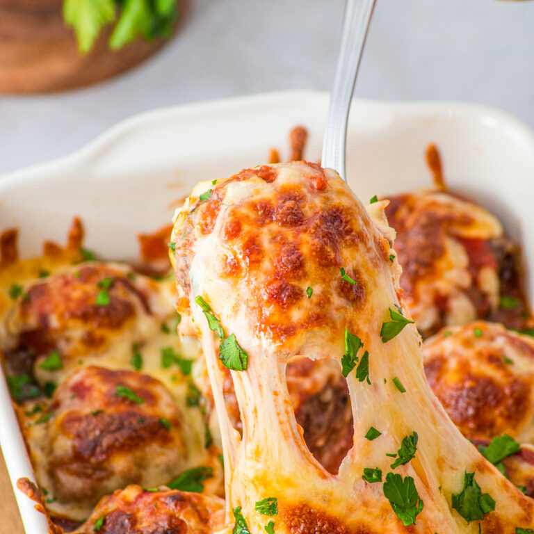 A cheesy meatball picked up with a spoon from a white serving dish.
