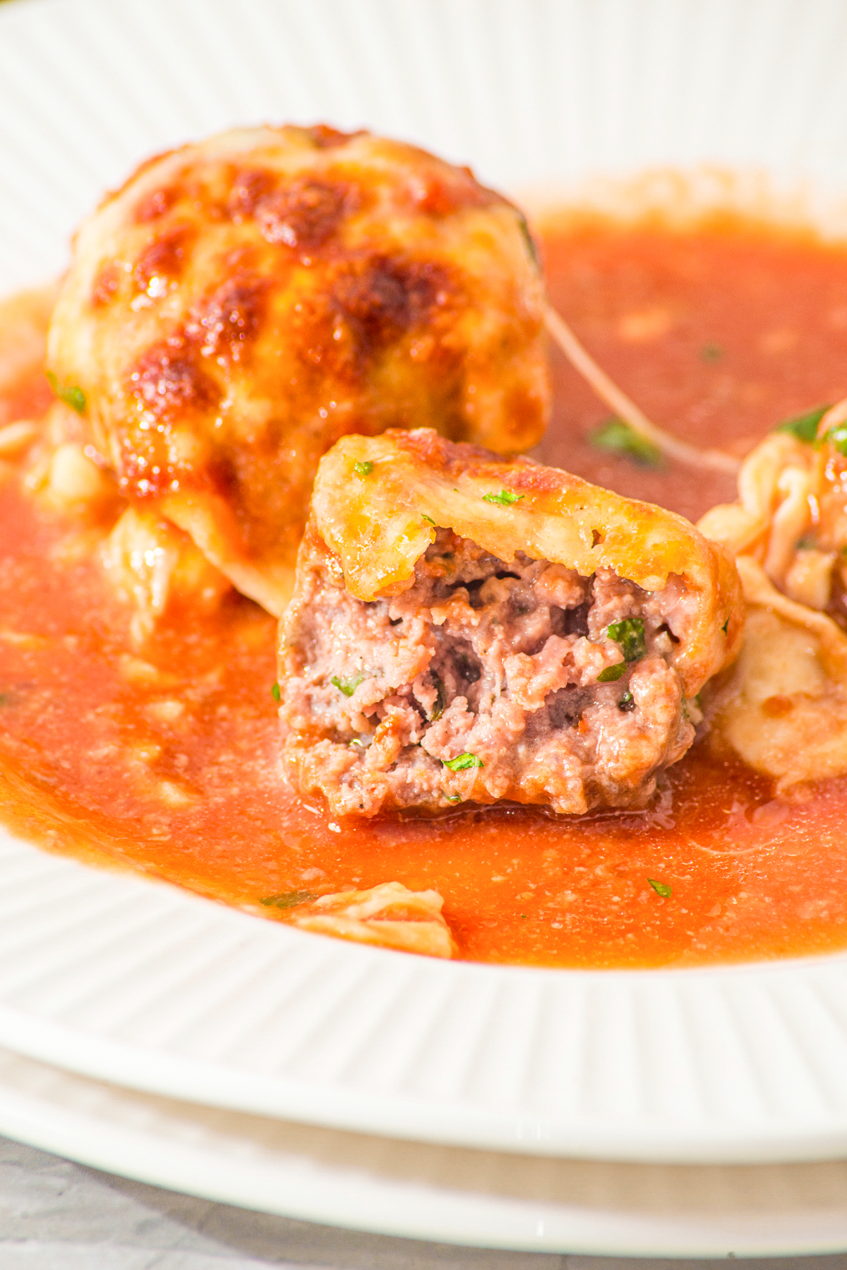 A single meatball in marinara sauce on a dish cut open showing the center.