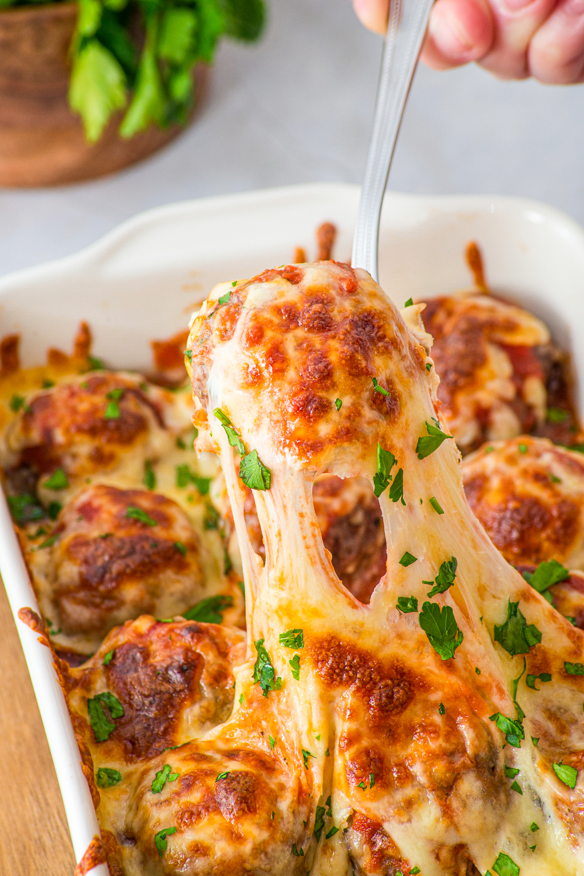 Serving a meatball from a baking dish with cheese pulling from the meatballs.