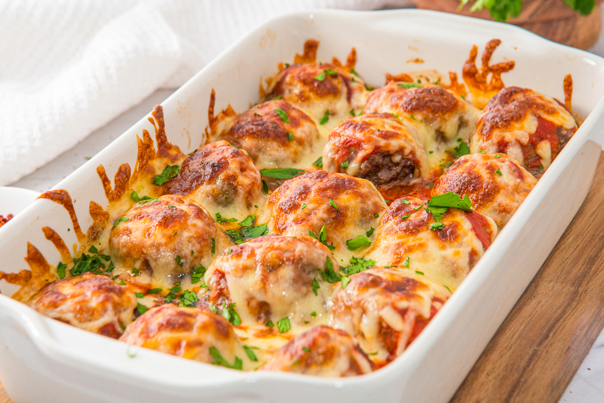 Baked meatballs in a white baking dish cooling on a wood trivet.