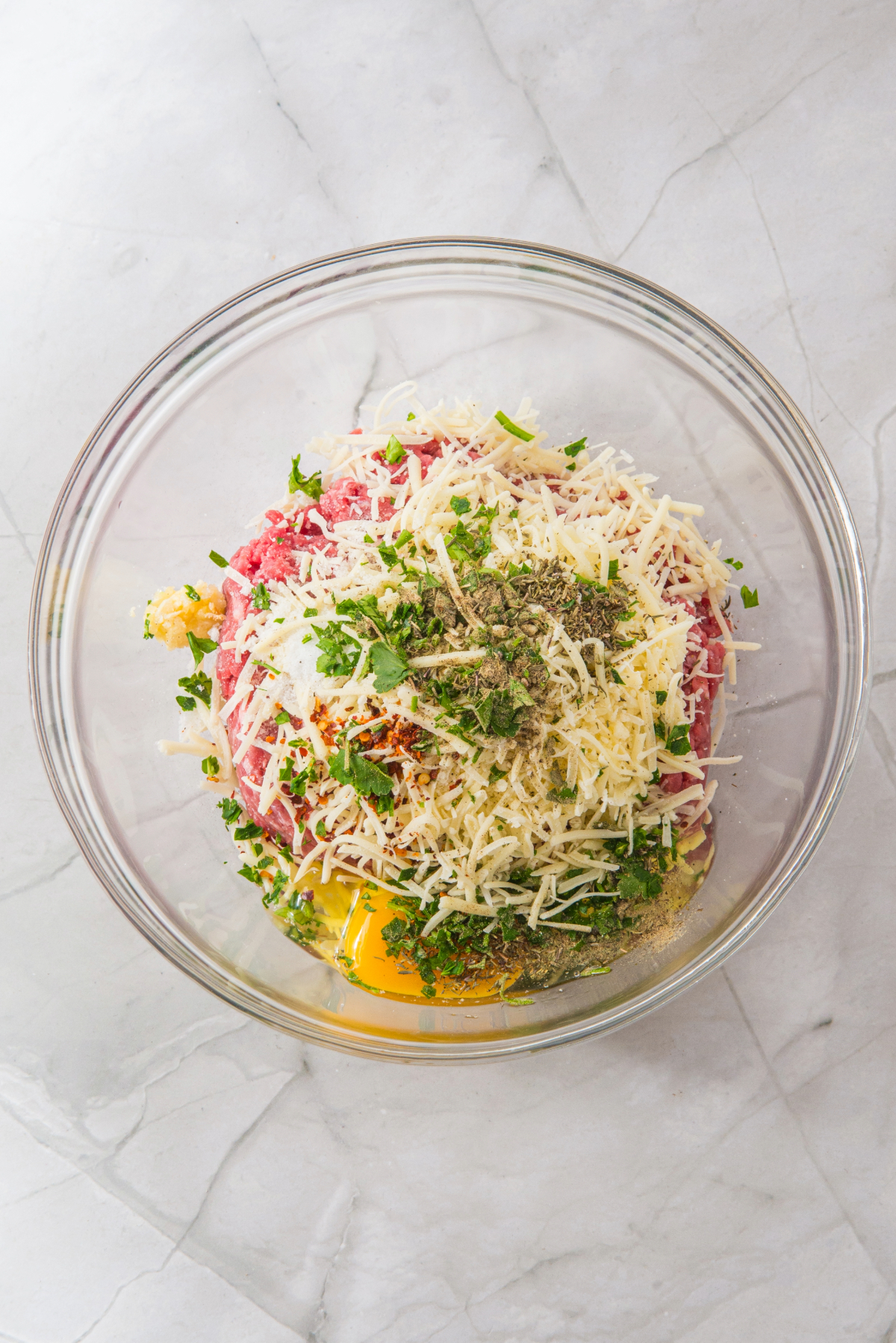 Ingredients to make meatballs in a clear mixing bowl.