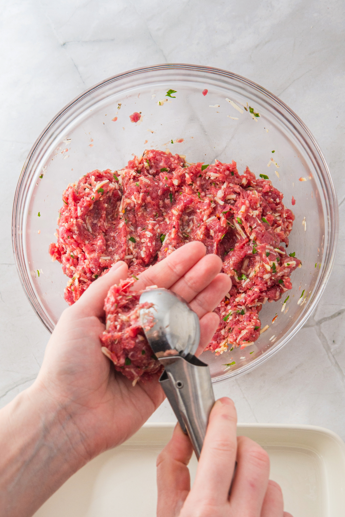 Forming ground beef into meatballs with a stainless steel scoop.