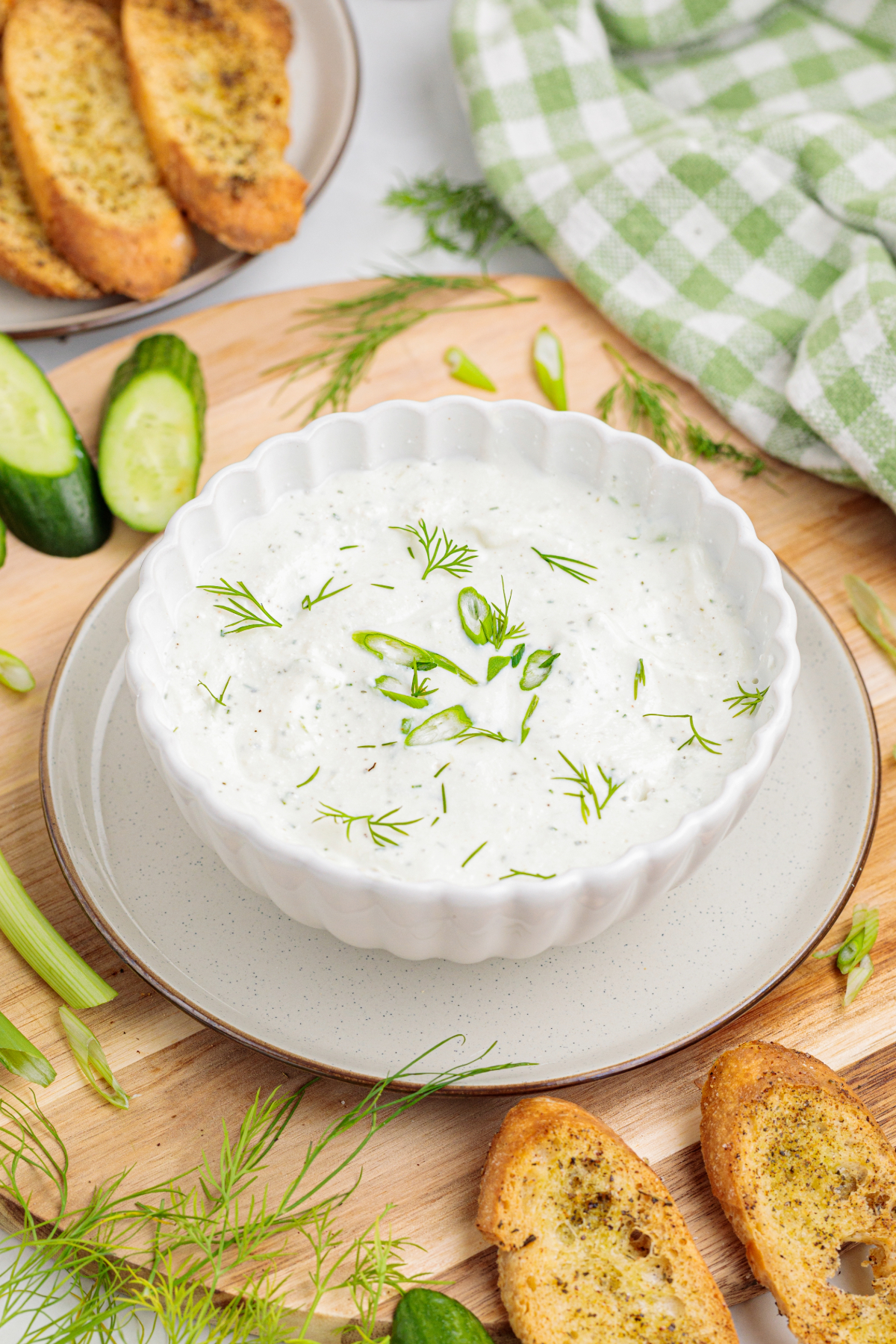 creamy dip topped with fresh dill in a bowl on a wooden cutting board.