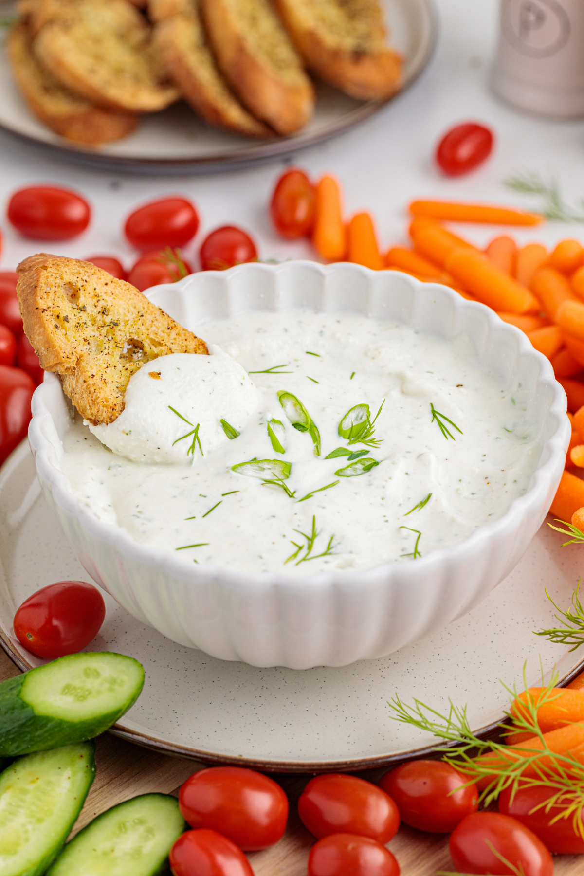 Homemade cottage cheese ranch dip in a white bowl on a white plate with vegetables around the plate.