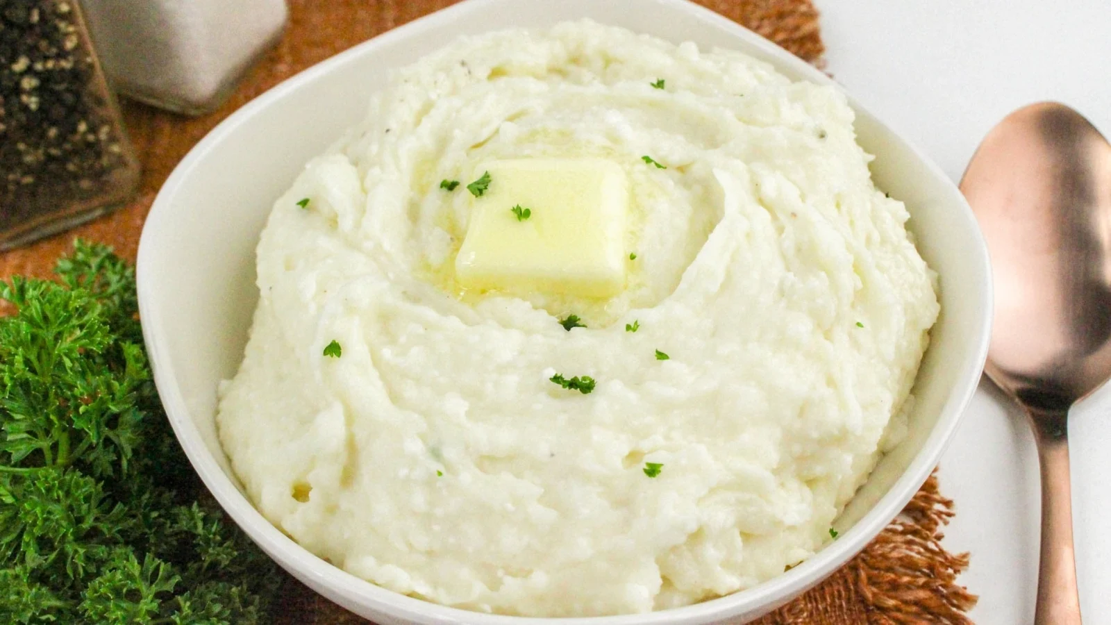 White bowl full of cottage cheese mashed potatoes topped with a pat of butter.