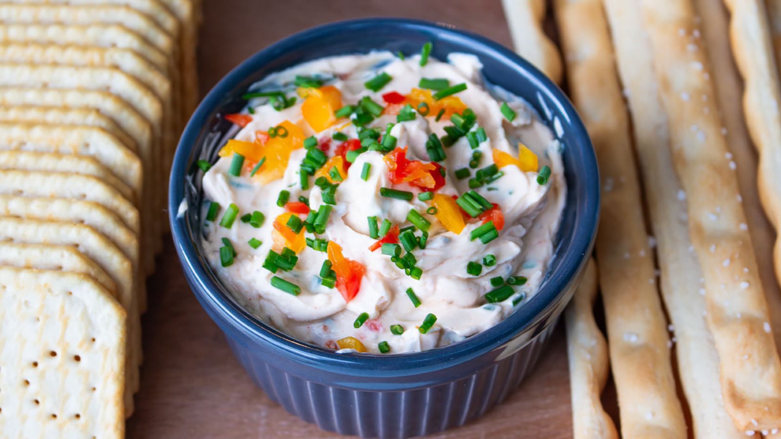 Bowl full of cream cheese dip and garnished with diced bell peppers and chives.