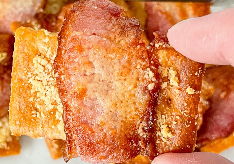 Fingers holding a bacon wrapped crackers.