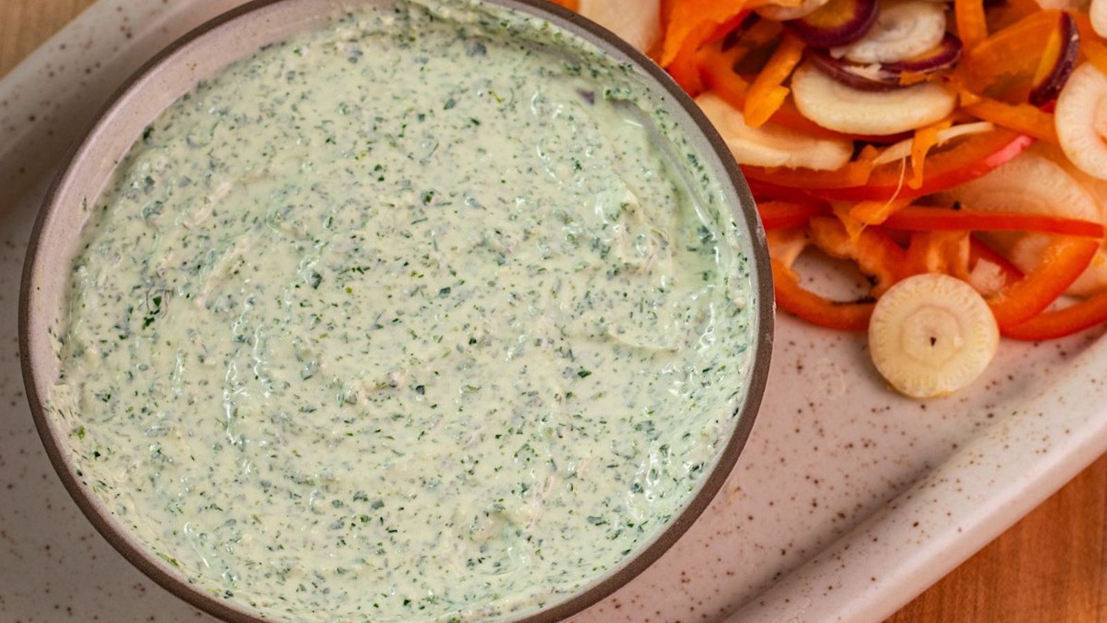 Glass bowl full of green goddess dressing on a table.