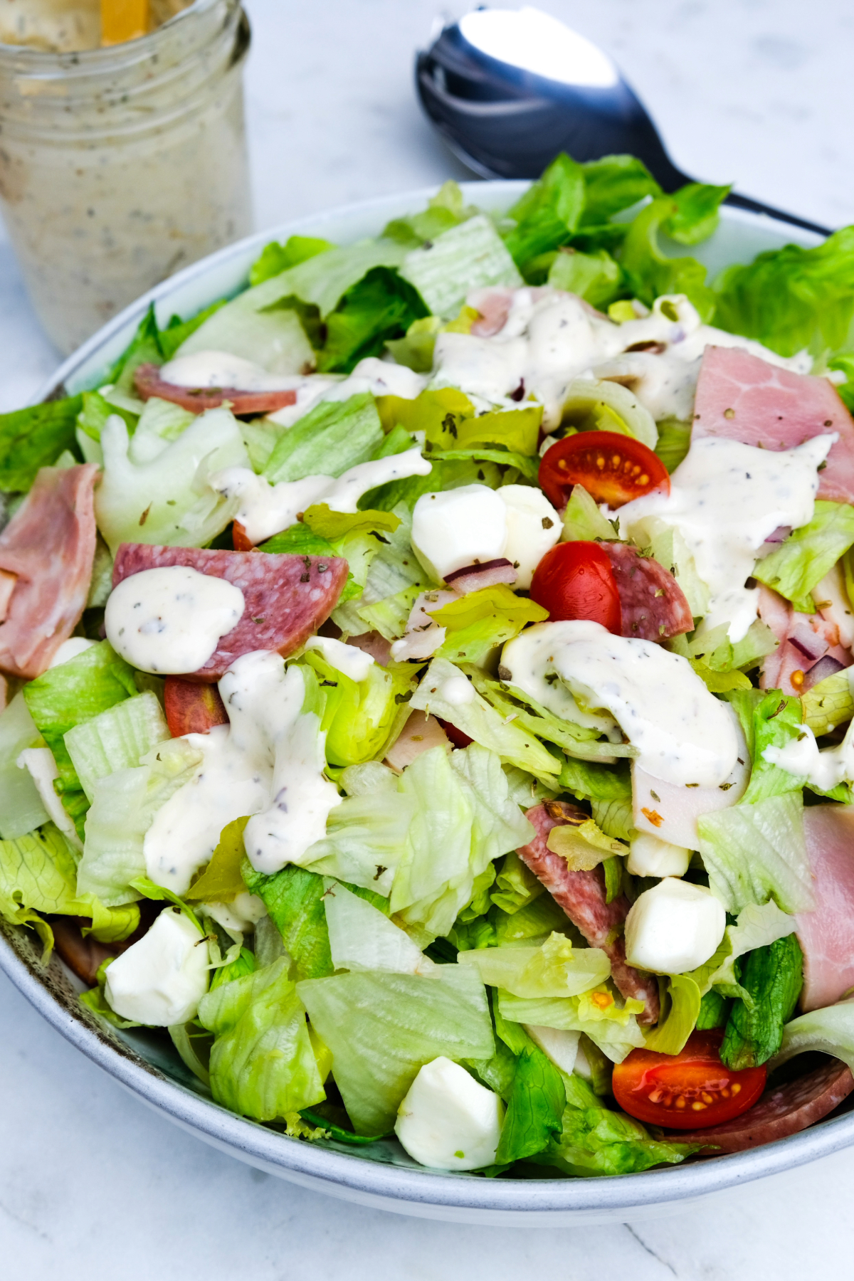 Tossed salad in a mixing bowl with dressing on top before tossing the salad.