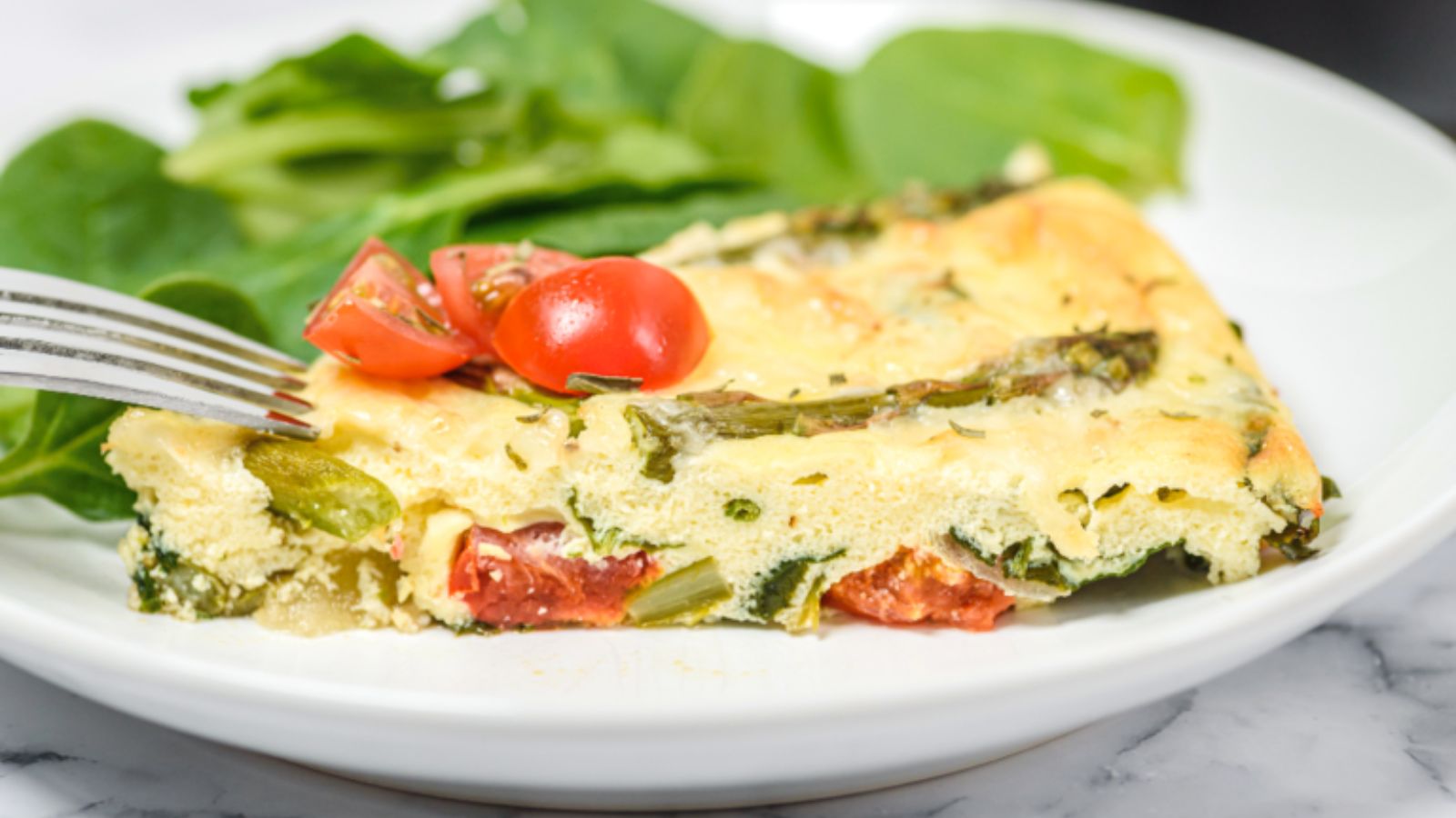 Slice of keto frittatta on a white plate topped with fresh tomatoes. 