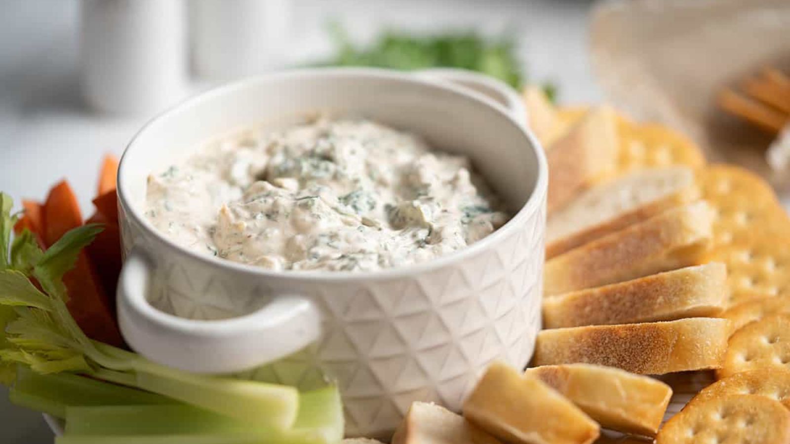 Bowl of lipton onion soup spinach dip. Surround by bread slices and crackers.