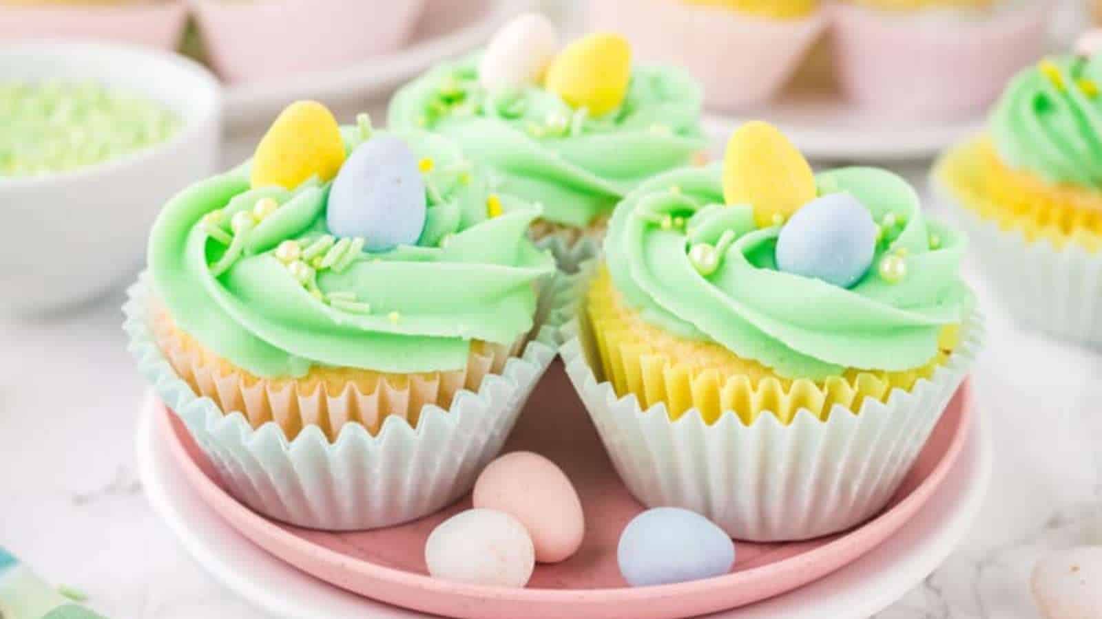 Three cupcake cakes on a pink plate topped with candy eggs.