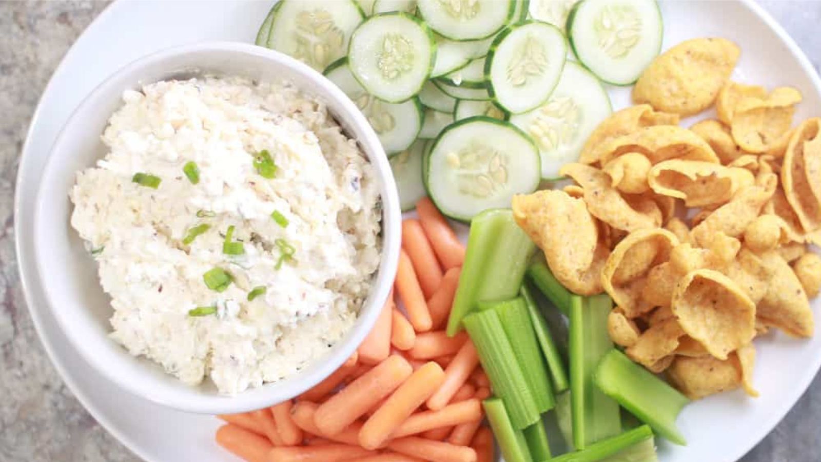 Bowl of cottage cheese dip on a plate with veggies and corn chips.