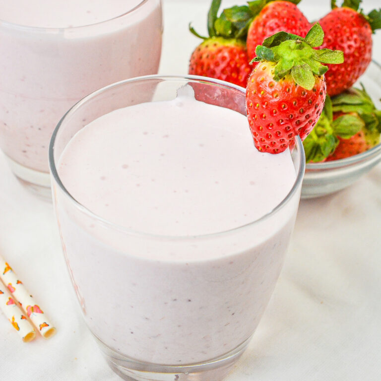 Strawberry smoothie in a clear glass with a strawberry on the side.