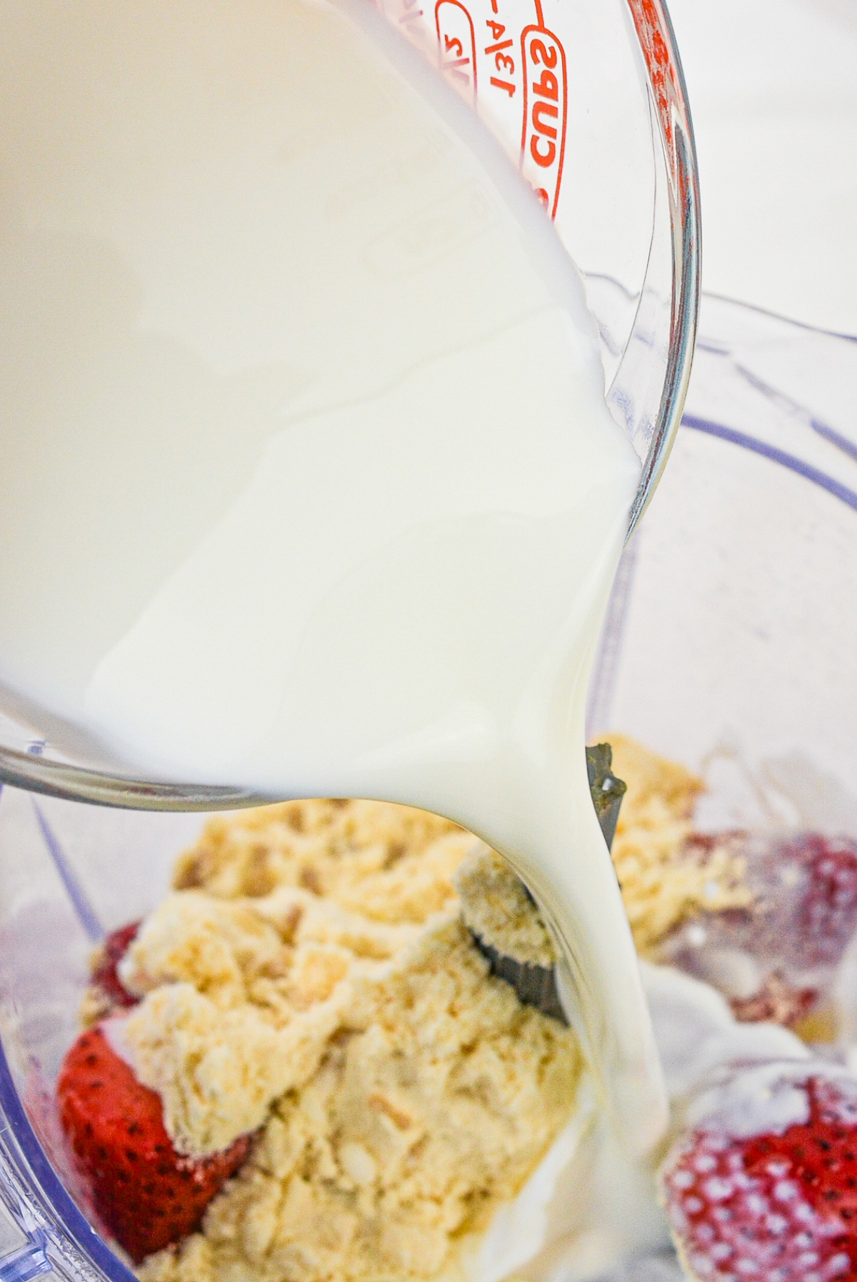 Almond milk in a measuring cup pouring into smoothie mixture.