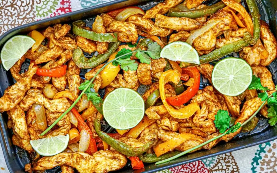 Sheet pan full of chicken fajitas topped with lime wedges.