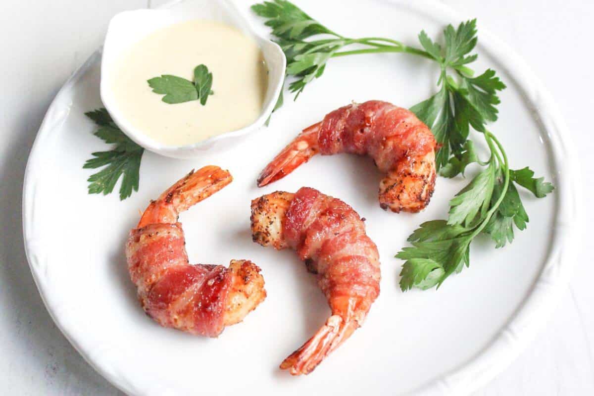 A bacon wrapped shrimp being held up over the platter of shrimp.