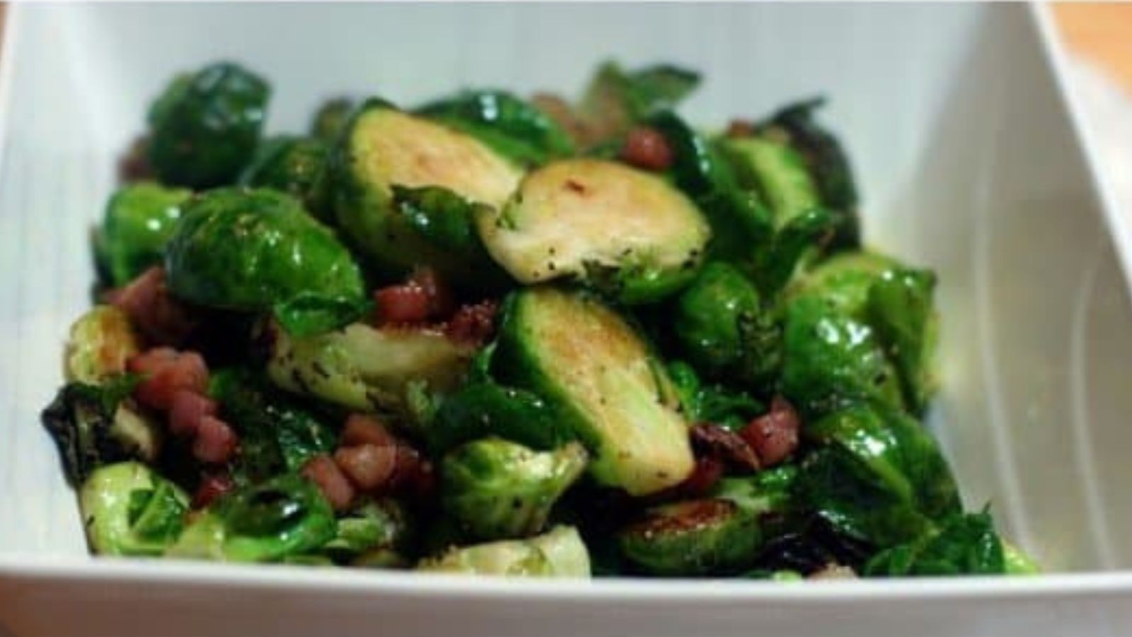 White bowl full of brussels and proscuitto. 