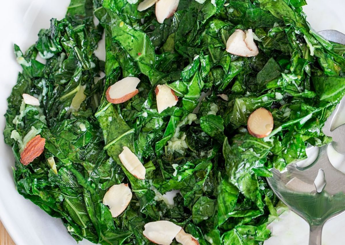 Serving of brussels sprouts tops and almonds in a large plate with a serving spoon. 